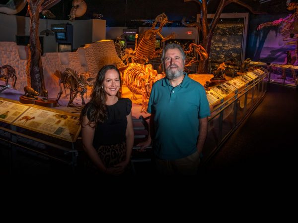 Two people stand in front of a panoramic fossil exhibit