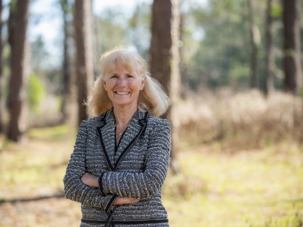 Person standing with arms crossed in a pine forest